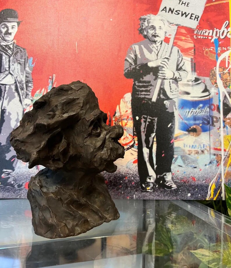 May include: A bronze sculpture of a person's head and shoulders. The sculpture is in a realistic style and has a textured surface. The sculpture is on a glass surface in front of a colourful painting.