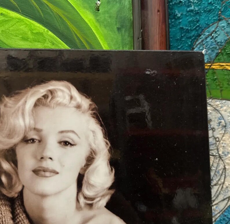 K&ouml;nnte beinhalten: Schwarz-Wei&szlig;-Fotografie von Marilyn Monroe mit ihrem charakteristischen blonden Haar und rotem Lippenstift. Das Bild ist ein Nahportr&auml;t, wobei die Person den Betrachter direkt ansieht. Das Foto ist von einem schwarzen Rahmen umgeben.