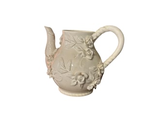 May include: White ceramic teapot with a floral design. The teapot has a curved handle and a spout. The floral design is embossed and features roses and leaves.