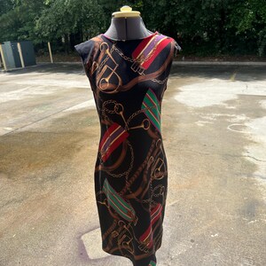 May include: A black sleeveless dress with a colorful print of equestrian-themed designs, including chains, stirrups, and belts.