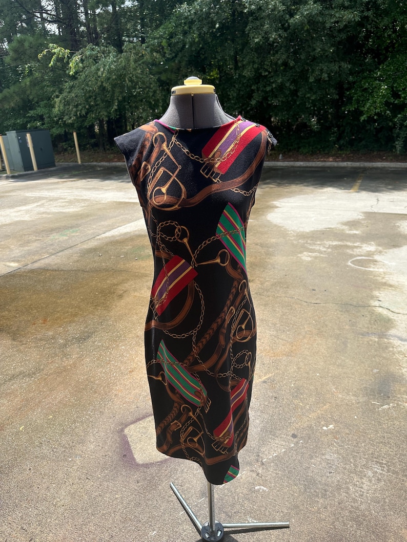 May include: A black sleeveless dress with a colorful print of equestrian-themed designs, including chains, stirrups, and belts.