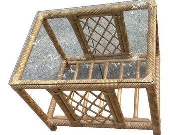 May include: A natural woven rattan end table with a glass top. The table has a lattice design on the sides and a shelf underneath.