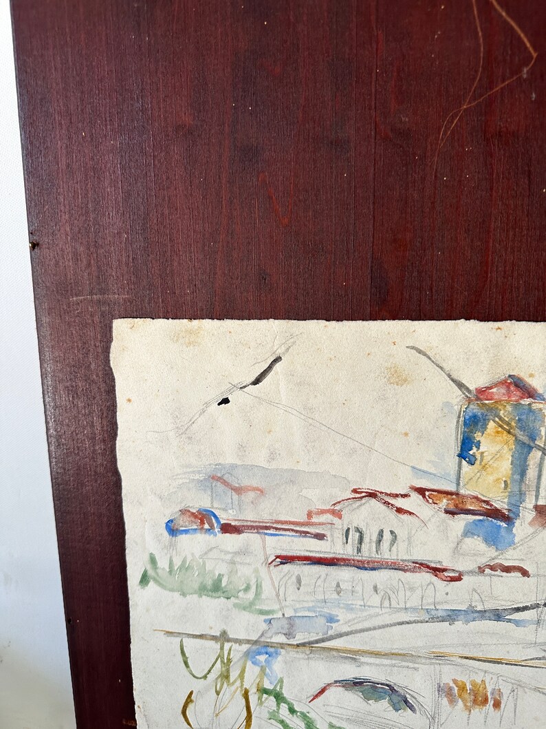 Puede incluir: Una pintura de acuarela de una ciudad con edificios y un cielo en tonos azules, verdes y marrones. La pintura est&aacute; enmarcada en un marco de madera oscura.