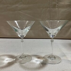 May include: Two clear martini glasses with a classic design. Each glass features a wide, triangular bowl, a slender stem, and a circular base. The glasses are made of transparent glass, perfect for cocktails.