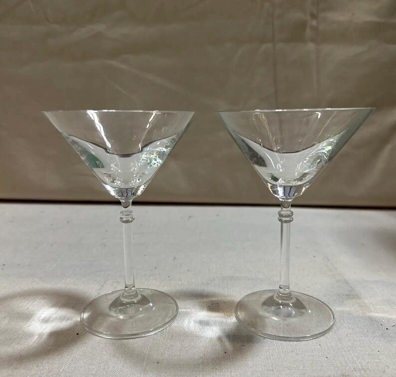 May include: Two clear martini glasses with a classic design. Each glass features a wide, triangular bowl, a slender stem, and a circular base. The glasses are made of transparent glass, perfect for cocktails.