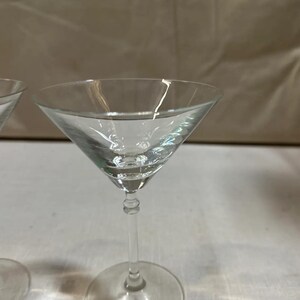 May include: A clear glass martini glass with a conical bowl, a long stem, and a circular base. The glass is transparent. The stem has a decorative design. Ideal for cocktails.