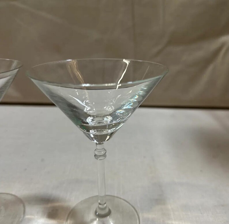 May include: A clear glass martini glass with a conical bowl, a long stem, and a circular base. The glass is transparent. The stem has a decorative design. Ideal for cocktails.