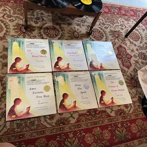 May include: Six vintage Newbery Award Records featuring illustrations of children reading books. The titles are "Up a Road Slowly", "Gay-Neck: The Tale of a Pigeon", "Amos Fortune, Free Man", "Across Five Aprils", "The Voyages of Doctor Dolittle", and "The Story of a Bad Boy".