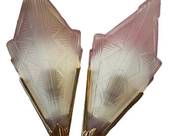 May include: A pair of wall sconces featuring diamond-shaped, frosted pink and white glass shades with geometric moulded patterns. Each glass shade is secured by a pointed gold-toned metal base at the bottom, creating a sharp, angular silhouette.