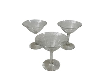 Op de afbeelding: Drie heldere cocktailglazen met stelen. De glazen hebben een ronde komvorm met geëtste patronen. De stelen zijn slank en de bases zijn cirkelvormig. De glazen zijn in een driehoekige formatie gerangschikt tegen een witte achtergrond.