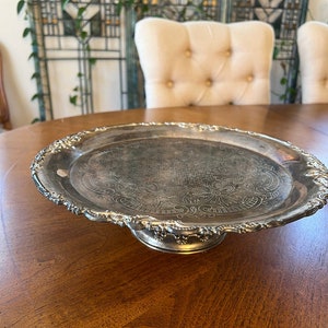 May include: A silver serving tray with a decorative embossed design and a raised pedestal base.