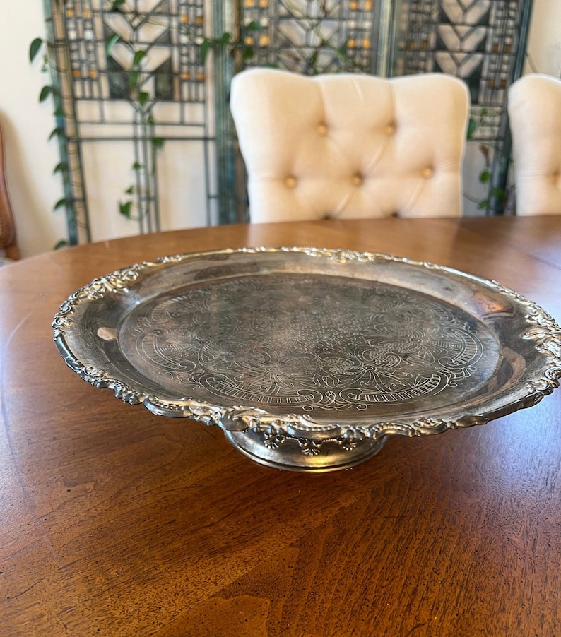 May include: A silver serving tray with a decorative embossed design and a raised pedestal base.