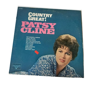 May include: A vintage vinyl record album cover for Patsy Cline's "Country Great!" album. The cover is blue with pink text and a photo of Patsy Cline. The album includes songs like "That Wonderful Someone" and "Three Cigarettes".