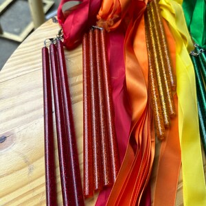 May include: Four red glitter wands with attached red satin ribbons and three orange glitter wands with attached orange satin ribbons. There are also yellow and green satin ribbons.