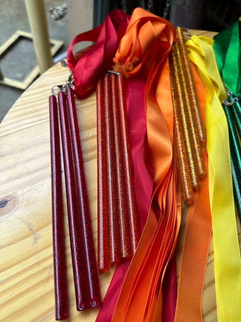 May include: Four red glitter wands with attached red satin ribbons and three orange glitter wands with attached orange satin ribbons. There are also yellow and green satin ribbons.