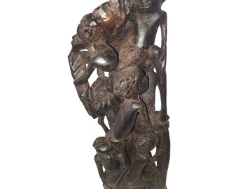 May include: A dark brown wooden sculpture of multiple figures, carved in a layered style, with the figures intertwined and overlapping.