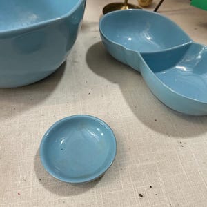 May include: A collection of light blue ceramic serving dishes. The set includes a large bowl, a divided serving dish, and a small round dish. The dishes have a glossy finish and a simple, classic design, suitable for serving snacks or appetizers.
