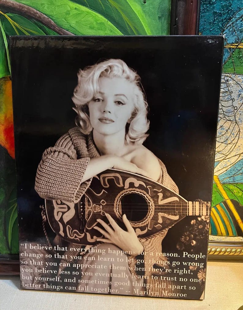 K&ouml;nnte beinhalten: Schwarz-Wei&szlig;-Druck mit Marilyn Monroe, die eine Laute h&auml;lt. Das Bild enth&auml;lt ein Zitat von Monroe: "Ich glaube, dass alles aus einem Grund geschieht..." Der Druck hat einen dunklen Hintergrund und ist gerahmt.