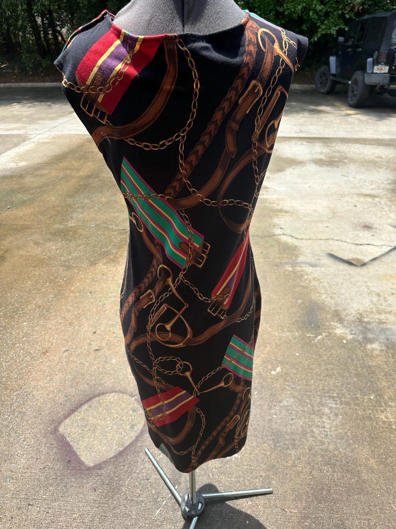 May include: A black sleeveless dress with a colorful pattern of gold chains, brown belts, and red, green, and purple stripes.