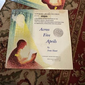 May include: A vintage record album cover featuring a young girl reading a book. The cover is yellowed with age and has a title that reads "Across Five Aprils" by Irene Hunt. The album is a recorded dramatization of the Newbery Medal Award book.