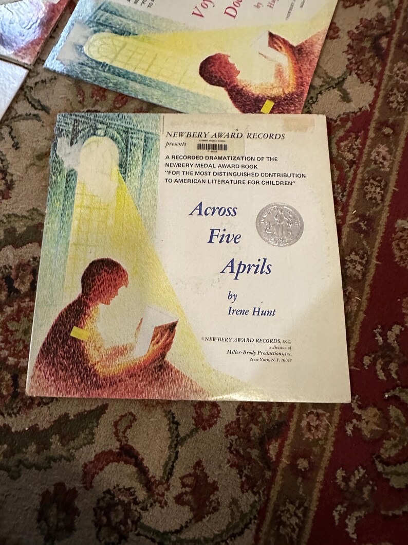 May include: A vintage record album cover featuring a young girl reading a book. The cover is yellowed with age and has a title that reads "Across Five Aprils" by Irene Hunt. The album is a recorded dramatization of the Newbery Medal Award book.