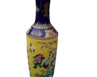 Puede incluir: Un jarrón de cerámica alto y delgado, de color azul y amarillo, con una boca ancha y un cuello estrecho. El jarrón está decorado con ribetes dorados y motivos florales, incluyendo un par de grullas. El jarrón tiene caracteres chinos en el lateral.
