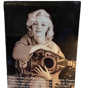 K&ouml;nnte beinhalten: Schwarz-Wei&szlig;-Fotografie von Marilyn Monroe mit einem Saiteninstrument. Sie tr&auml;gt einen strukturierten Pullover. Das Bild enth&auml;lt ein Zitat von Marilyn Monroe.