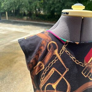 May include: A black sleeveless top with a gold chain and horse bit print. The top has a green and pink trim around the neckline.