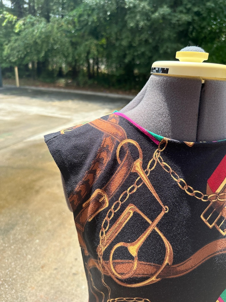 May include: A black sleeveless top with a gold chain and horse bit print. The top has a green and pink trim around the neckline.