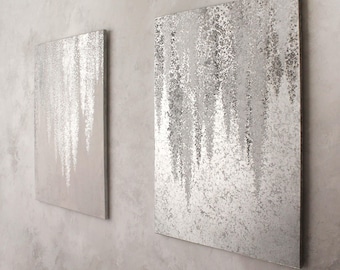 May include: Two rectangular wall art pieces with a silver, textured design resembling falling rain. The artwork is mounted on a light grey wall, creating a modern and minimalist aesthetic. The silver design contrasts with the neutral background.
