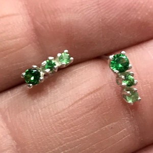 May include: A pair of silver earrings with a graduated row of green gemstones. The earrings are small and delicate.