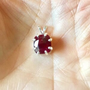 May include: A red gemstone pendant with a silver setting. The pendant is on a white background.