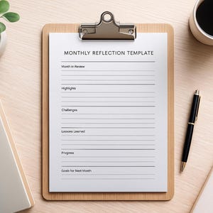 Puede incluir: Un portapapeles de madera con una hoja blanca impresa con "MONTHLY REFLECTION TEMPLATE". Un bolígrafo negro, una taza de café, una pequeña planta en maceta y un cuaderno cerrado están sobre una superficie de madera clara.