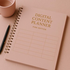 Puede incluir: Un planificador de contenido digital rosa, edición rosa, con letras doradas y encuadernación en espiral. Un bolígrafo negro y una taza rosa están junto al planificador. El planificador tiene un diseño de cuadrícula para la planificación de contenido.