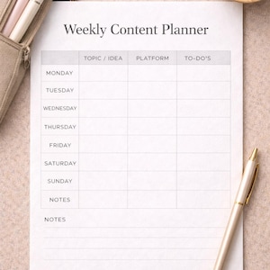 Puede incluir: Un planificador de contenido semanal con secciones para tema/idea, plataforma y tareas. Un bolígrafo dorado, un pequeño cuenco de madera con clips rosas y un estuche beige con bolígrafos también están presentes.