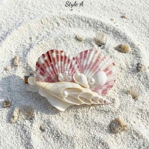 Könnte beinhalten: Haarspange mit Muscheln, darunter zwei rosa-weiße Jakobsmuscheln, kleine weiße Muscheln und Kunstperlen. Der Clip liegt auf weißem Sand, mit dem Text "Style A" in der oberen linken Ecke.
