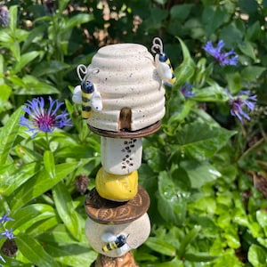 May include: A vertical garden stake featuring a ceramic beehive top with two attached bees, followed by a stack of alternating round and cylindrical ceramic beads in cream, yellow, and brown, decorated with embossed leaf and floral patterns.
