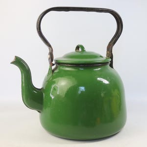 May include: A glossy, forest green enamel tea kettle with a rounded body, a curved spout, and a matching lid. The kettle features a sturdy, dark-colored metal handle that arches over the top, attached with visible rivets on both sides.