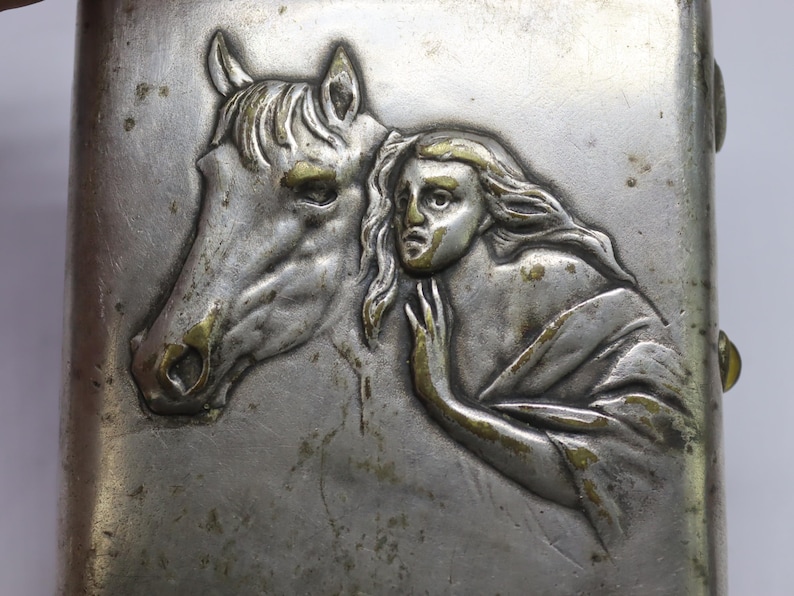 May include: Silver-toned metal case with a detailed relief of a horse's head and a woman. The horse's features are highlighted with gold accents, as is the woman's hair and clothing. The woman's expression is one of concern, and she is touching the horse.