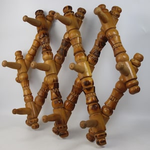 Könnte beinhalten: Ein ausziehbarer Wandhaken aus Holz mit einem Gitterdesign und mehreren hervorstehenden Haken. Das Gestell besteht aus hellbraunem Holz mit dunkleren, gebeizten Akzenten an den gedrechselten, dekorativen Elementen des Rahmens und der Haken.