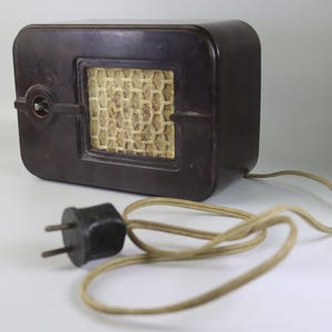 May include: A vintage brown radio with a rectangular shape and rounded edges. The front features a speaker grille with a woven pattern. A power cord and plug are visible. This antique radio is a classic piece of electronics.