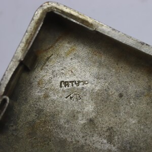 May include: Close-up of a rectangular, silver-toned metal object. The interior surface has a textured appearance with the word "PATYHO" and a symbol with the number "13" etched into the metal.