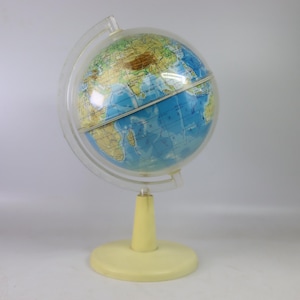 Puede incluir: Un globo terráqueo vintage con un meridiano de plástico transparente y una base y soporte de color amarillo claro. El globo presenta un mapa detallado con océanos azules y continentes en tonos verdes, marrones y amarillos. Una herramienta educativa clásica.