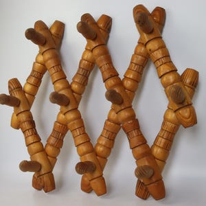 Könnte beinhalten: Ein ausziehbarer Wandgarderobenständer aus Holz mit einem Gitterdesign und mehreren Haken. Das Gestell besteht aus hellbraunem Holz mit einer natürlichen Maserung und setzt sich aus miteinander verbundenen Segmenten in Rautenform zusammen.
