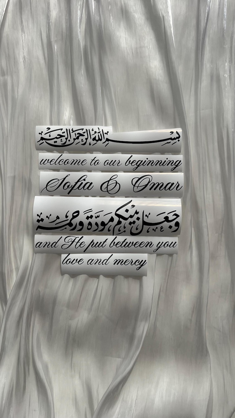 May include: White rectangular decals with black calligraphy and English text. The decals read "welcome to our beginning", "Sofia & Omar", and a quote about love and mercy. The background is a white, textured fabric.