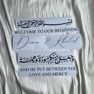 May include: White rectangular stickers with black calligraphy and text. The stickers include phrases in Arabic and English, such as "Welcome to Our Beginning," "Dania & Khaled," and "Love and Mercy."