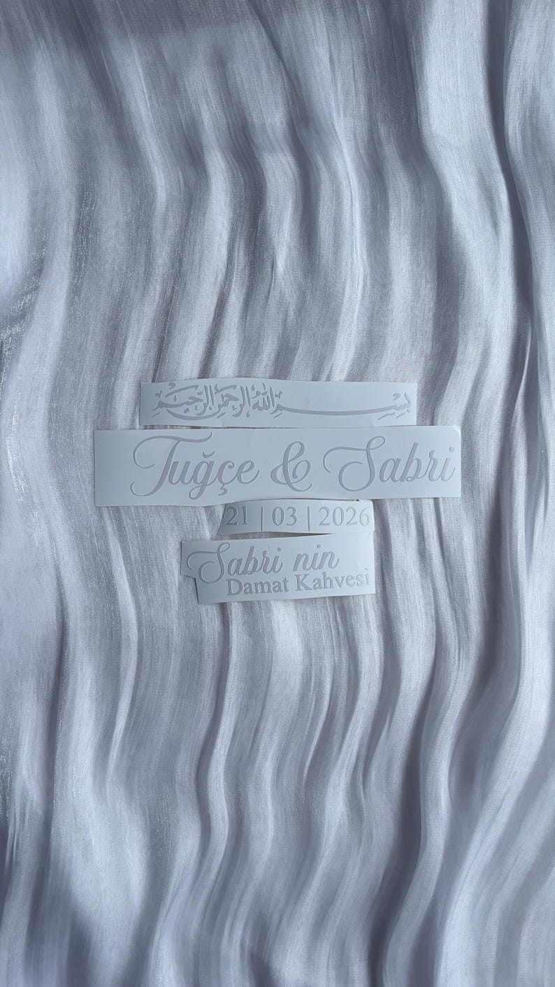 May include: White stickers with elegant script text on a textured white background. The stickers include names, a date, and the phrase "Sabri nin Damat Kahvesi". The overall theme is wedding or celebration.