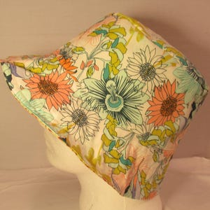 May include: A white fabric hat with a floral print featuring pink, green, blue, and yellow flowers. The hat has a wide brim and a rounded crown.