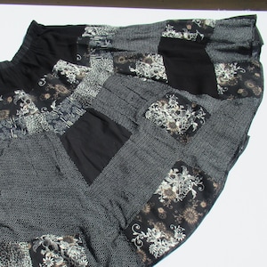 May include: A patchwork skirt featuring a variety of patterns and textures. The skirt combines black, white, and gray fabrics, including polka dots, floral prints, and solid panels. The waistband is black and elasticized.