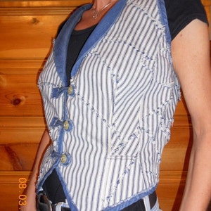 May include: A blue and white striped vest with a denim collar and trim. The vest has a button closure and is made of a patchwork fabric.
